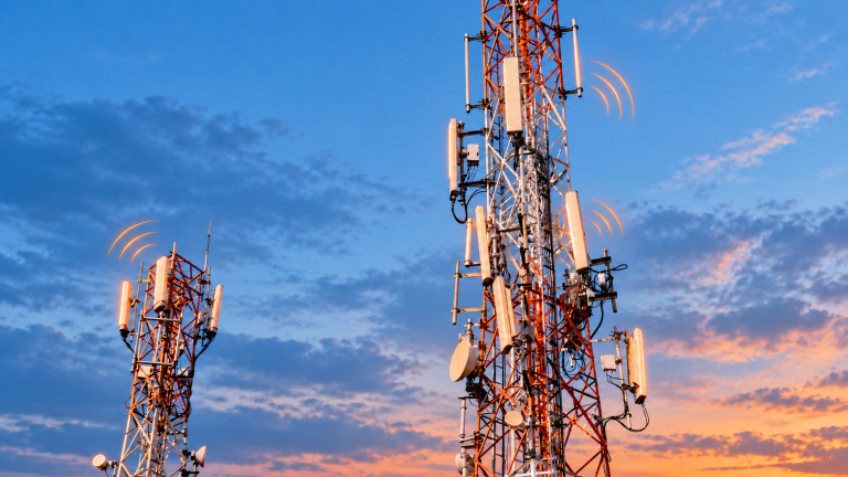 Two telecom towers with orange wireless signal indicators against a blue evening sky.